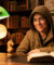 Une personne en sweat à capuche sourit devant un échiquier et un livre dans une bibliothèque au style classique.