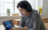 Un jeune homme portant un casque audio étudie l'anglais sur une tablette dans un intérieur lumineux.