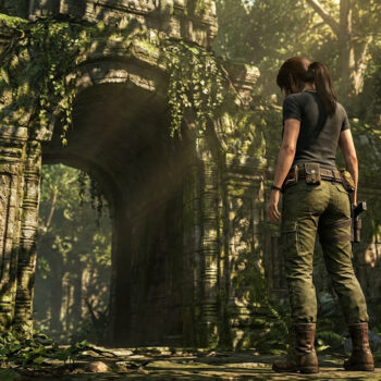 Lara Croft debout de dos devant une arche de pierre ancienne recouverte de végétation dans une jungle luxuriante.