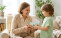 Un jeune garçon souriant offre un cadeau emballé avec une carte en forme de cœur à sa grand-mère souriante.