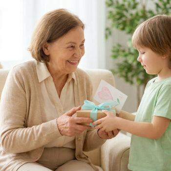 Un jeune garçon souriant offre un cadeau emballé avec une carte en forme de cœur à sa grand-mère souriante.