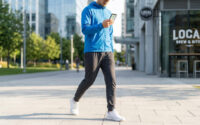 Un homme en veste bleue marche en ville en consultant son itinéraire sur son smartphone.