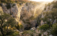 Un randonneur contemple le gouffre impressionnant de l'Igue de Goudou baigné par la lumière dorée du soleil.