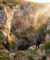 Un randonneur contemple le gouffre impressionnant de l'Igue de Goudou baigné par la lumière dorée du soleil.