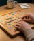 Mains plaçant les lettres du mot VET sur un plateau de Scrabble en bois. D'autres mots, une lampe, une tasse et un sac Scrabble sont visibles.