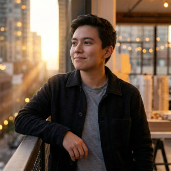 Jeune homme souriant debout sur une terrasse au coucher du soleil avec une vue sur la ville en arrière-plan.