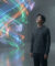 Un homme regarde avec émerveillement une spirale de lumière colorée et abstraite dans un espace minimaliste en béton.