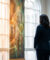 Une femme en tailleur sombre vue de dos, contemplant une fresque murale lumineuse dans un hall d'entrée.