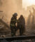 Un pompier aide une femme enveloppée dans une couverture à marcher au milieu des décombres fumants après une catastrophe.