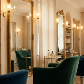Dans un institut de beauté, étagères de produits, miroirs dorés, fauteuils velours. Une coiffeuse s'occupe d'une cliente.