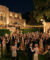 Une foule d'invités en tenues des années 20 danse et socialise lors d'une fête nocturne somptueuse devant un grand manoir.