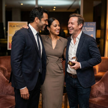 Trois personnes souriantes lors d'une réception, l'homme à droite tient un trophée de festival du film.