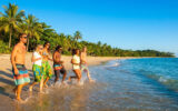 Un groupe d'amis souriants marche et court dans l'eau sur une plage tropicale au Brésil.