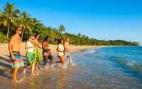 Un groupe d'amis souriants marche et court dans l'eau sur une plage tropicale au Brésil.