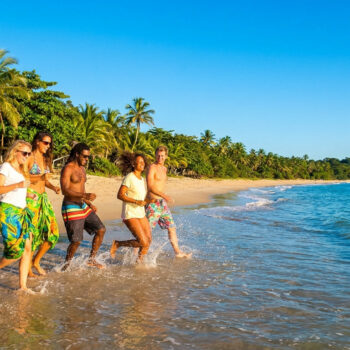 Un groupe d'amis souriants marche et court dans l'eau sur une plage tropicale au Brésil.