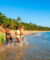 Un groupe d'amis souriants marche et court dans l'eau sur une plage tropicale au Brésil.