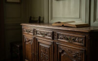 Un buffet en bois sculpté de style ancien avec un livre ouvert posé sur son plateau dans une pièce aux murs lambrissés.