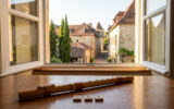 Une flûte en bambou appelée Nay posée sur une table en bois devant une fenêtre donnant sur un village historique.