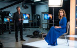 Un homme en costume et une femme en robe bleue sur le plateau technique d'une émission de télévision.