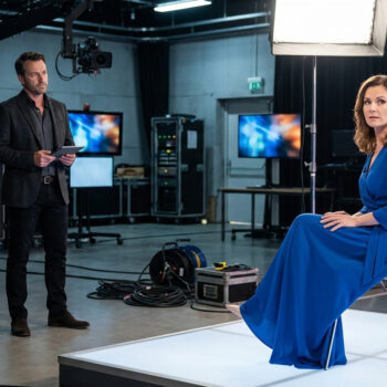 Un homme en costume et une femme en robe bleue sur le plateau technique d'une émission de télévision.