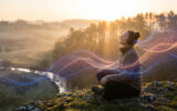 Une femme assise sur un rocher en pleine nature, écoutant de la musique avec des ondes lumineuses autour d'elle au coucher du soleil.