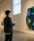 Une personne en blazer sombre observe une grande peinture abstraite colorée dans une galerie d'art moderne.