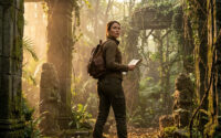 Une femme exploratrice avec un sac à dos et une carte dans un temple en ruine recouvert de mousse en pleine jungle.
