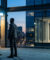 Deux hommes font face à un homme en costume derrière une vitre sur un toit terrasse au crépuscule.