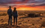 Un couple en tenues de cow-boy contemple un ranch au Texas sous un spectaculaire coucher de soleil.