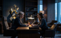 Deux femmes se font face à un bureau dans un bureau sombre et luxueux avec une lampe de table éclairée.