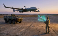 Un soldat utilise une tablette pour piloter un drone de reconnaissance au-dessus d'un véhicule blindé au coucher du soleil.