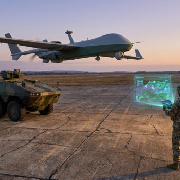 Un soldat utilise une tablette pour piloter un drone de reconnaissance au-dessus d'un véhicule blindé au coucher du soleil.