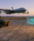 Un soldat utilise une tablette pour piloter un drone de reconnaissance au-dessus d'un véhicule blindé au coucher du soleil.