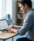 Un homme souriant travaille sereinement sur son ordinateur portable dans un bureau lumineux.