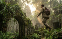 Nathan Drake avec un sac à dos sautant devant des ruines antiques envahies par la végétation dans une jungle lumineuse.