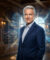 Portrait d'un homme élégant en costume devant une bibliothèque, entouré d'hologrammes de télévisions et de dragons.