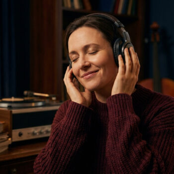 Femme écoutant de la musique avec un casque audio les yeux fermés dans un salon confortable.