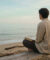 Un homme assis sur un banc en bois sur la plage, regardant l'océan avec un livre sur ses genoux.