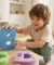 Un jeune enfant souriant joue avec des lettres colorées en mousse sur une petite table en bois dans une chambre.