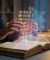 Un homme manipule une interface holographique de symboles au-dessus d'un livre ouvert sur un bureau.
