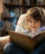 Un jeune garçon assis dans un fauteuil lit un livre d'où s'échappent des fées lumineuses et des notes de musique.