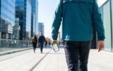 Un homme marche dans une rue moderne en consultant l'application Mappy sur son smartphone pour s'orienter.